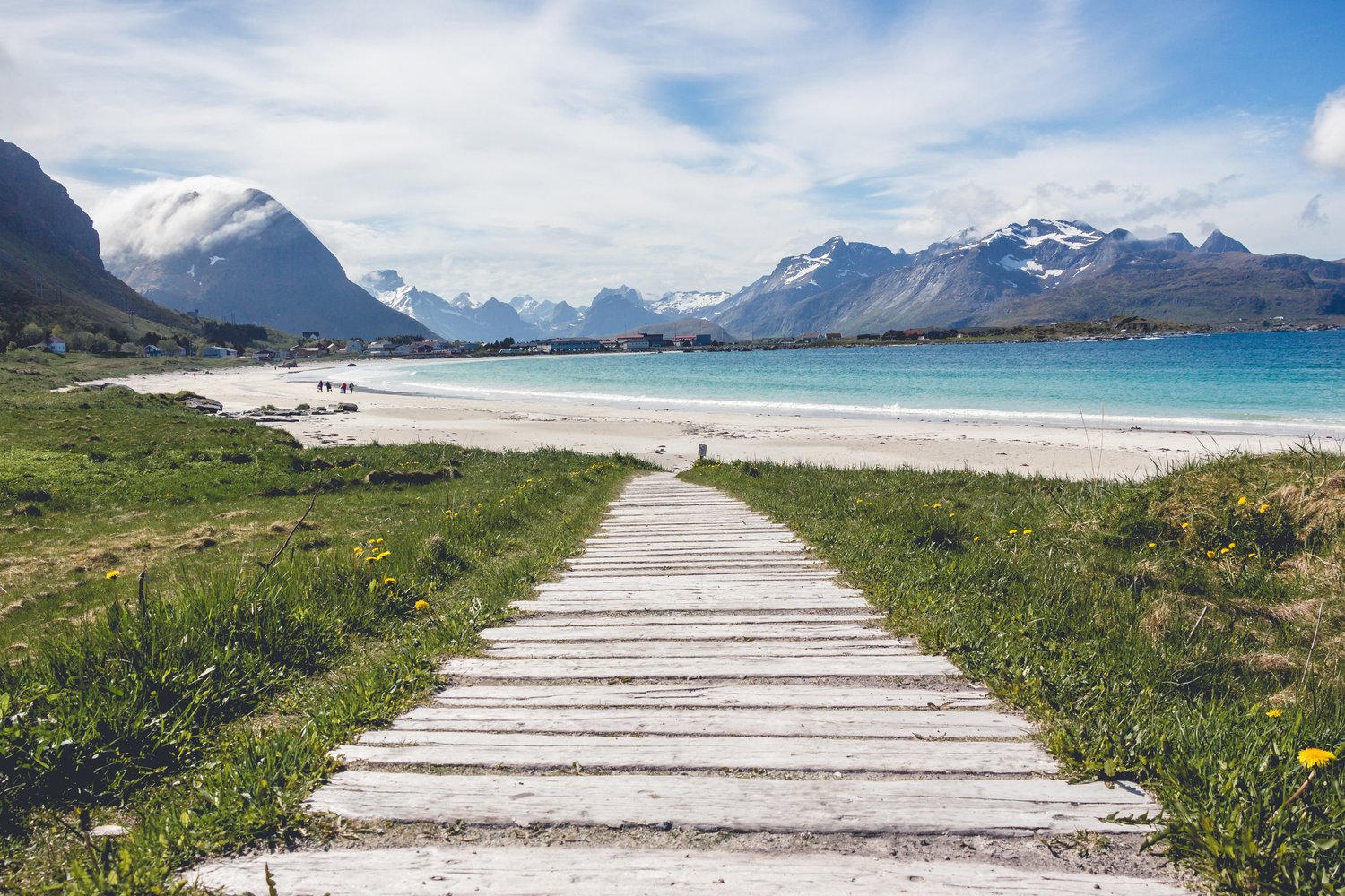A wooden boardwalk through the grass to a sandy beach, with mountains beyond